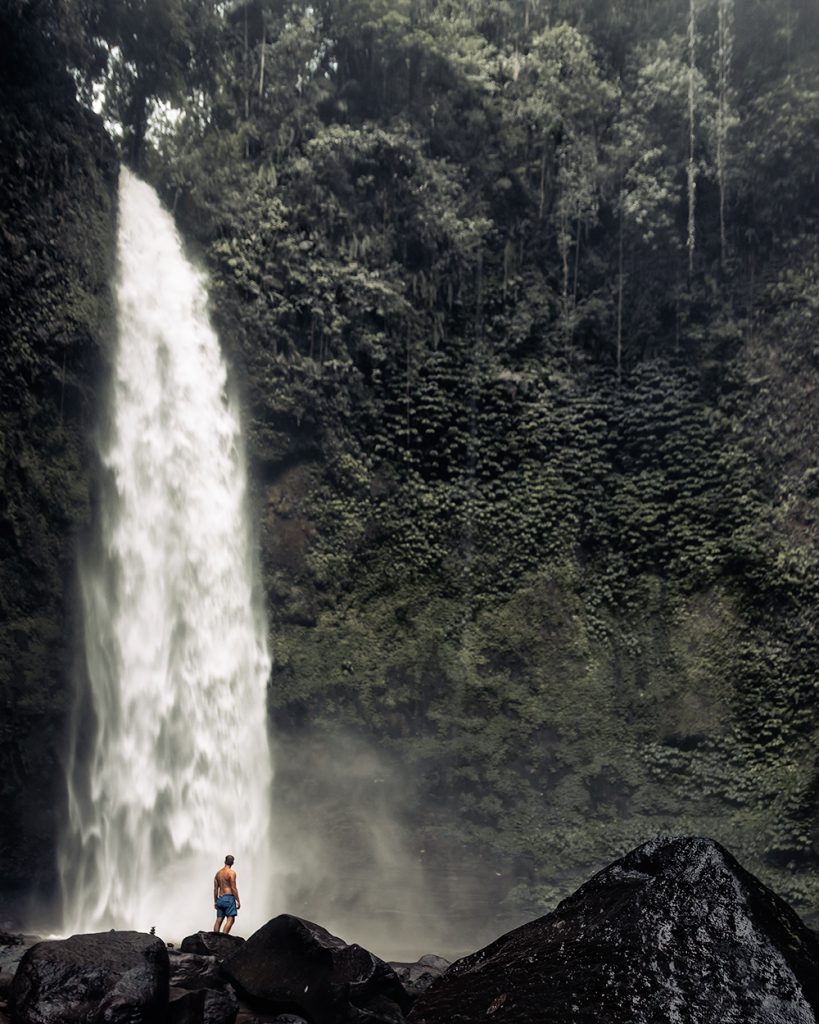 Man gazing up at tropical waterfall
